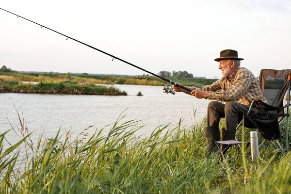 Vista lateral sobre o homem idoso pesca no lago na natureza, paciência e conceito de recreação — Fotografia de Stock