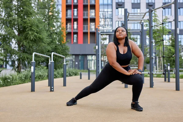 focused fat woman in black tracksuit is engaged in fitness on sports ground, side view portrait