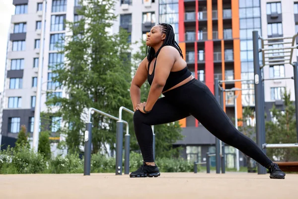 beautiful fat woman in black tracksuit is engaged in fitness on sports ground, side view portrait