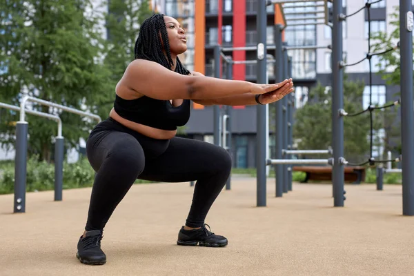Plus size fat afro american woman squats in sports ground. Weight losing, obesity — Stock Photo, Image