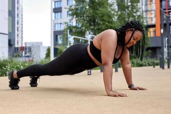 Siyah spor giyimli obez bir kadın, spor yapıyor, şınav çekiyor ya da şınav çekiyor. — Stok fotoğraf