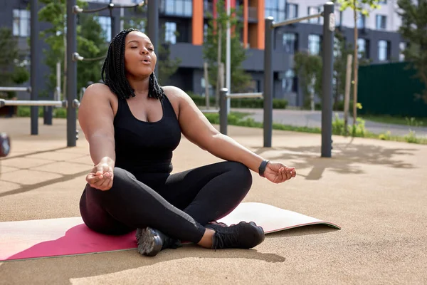Nilüfer pozisyonunda yoga minderinde oturan spor elbiseli, barışçıl melez ırk kadını. — Stok fotoğraf
