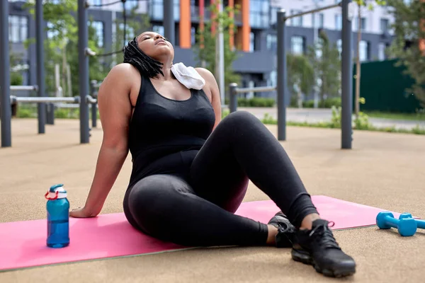 Træt overvægtige afro kvindelige have hvile på fitness mat efter træning, tage en pause - Stock-foto