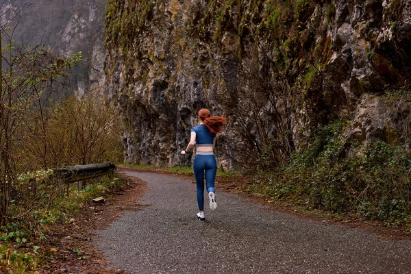 Visão traseira na ruiva senhora modelo desportivo correndo nas montanhas, ao longo da estrada — Fotografia de Stock