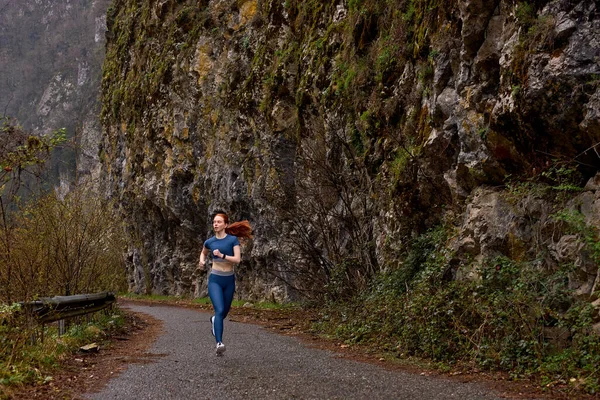 Spor kıyafetli güzel bir bayan dağlarda koşu antrenmanı yapıyor. — Stok fotoğraf