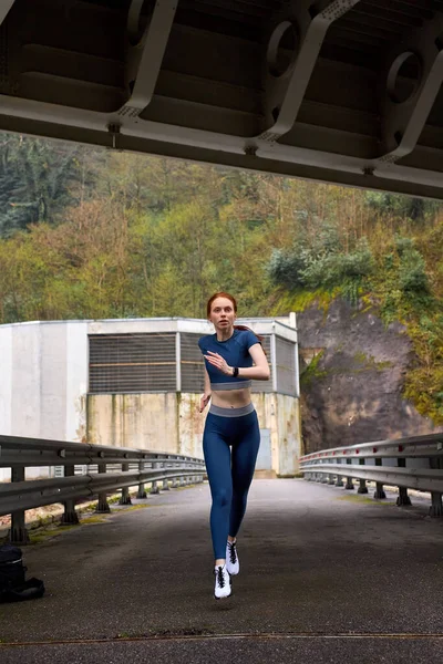 Portret roodharige leuke vrouw joggen op de brug alleen in de ochtend, kopiëren ruimte — Stockfoto