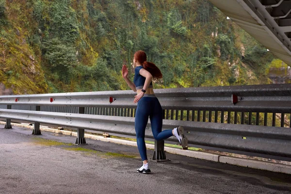 Rear view On Fit red-haired Powerful lady jogging on modern bridge, view from back — Stock Photo, Image