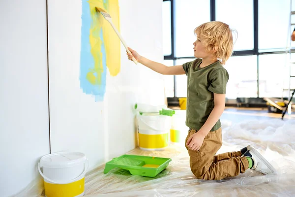 Pequeño niño pintura pared con rodillo. El color de la pintura es azul claro y amarillo. Habitación en casa —  Fotos de Stock