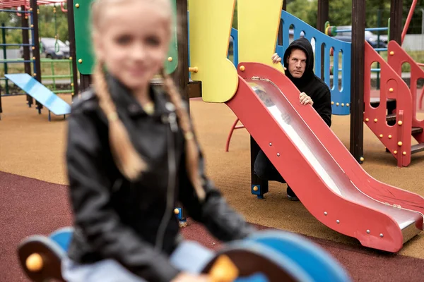 Terrible threatening pedophile spies on child girl while having fun in playground — Stock Photo, Image