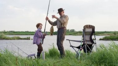 Erkek aile balıkçılığı. Dedenle birlikte yaz nehrinde balık tutan bir çocuk.