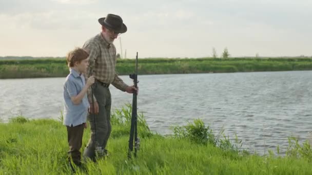Side view on happy senior grandfather and grandson in nature came on lake to fish — Stock Video