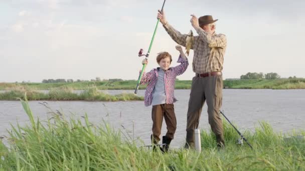 Щасливий усміхнений маленький хлопчик з його першим лососем на прісноводній риболовлі з дідом — стокове відео