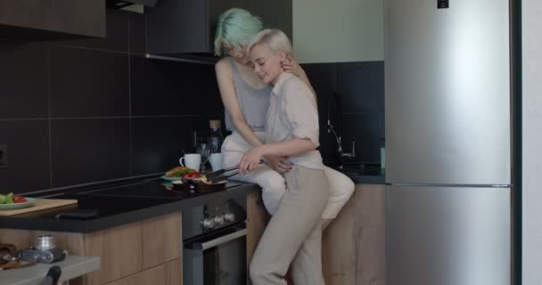 Zwei lesbische Freundinnen frühstücken in der Küche, küssen und umarmen sich. Lebensstil der Menschen — Stockvideo