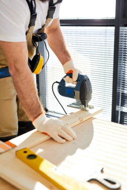 Erkek inşaat işçisi evi yenilerken elektrikli testereyle tahta kesiyor.