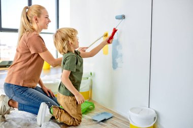 Mutlu anne küçük sevimli çocuğa boya fırçasıyla duvar boyamayı öğretiyor.