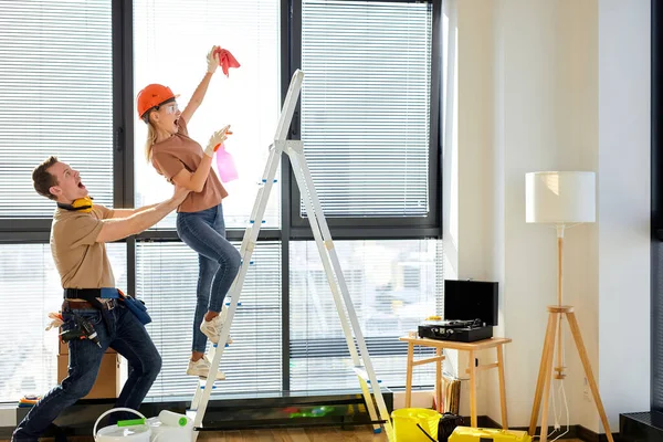 Engraçado homem apoio esposa de volta enquanto a fêmea está limpando teto na escada rolante — Fotografia de Stock