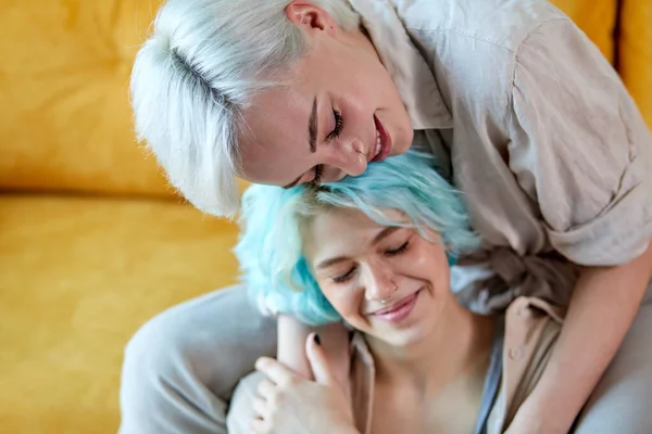 Feliz lesbianas pareja tener resto en casa abrazando en sofá en acogedor habitación — Foto de Stock