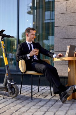 Resmi giyinmiş kendine güvenen bir iş adamı açık kafede dizüstü bilgisayarla çalışır.