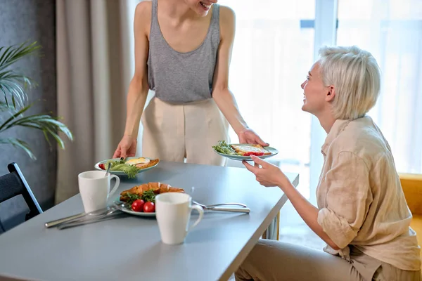 Positive caucasienne dame lesbienne traite petite amie avec petit déjeuner, le matin à la maison — Photo