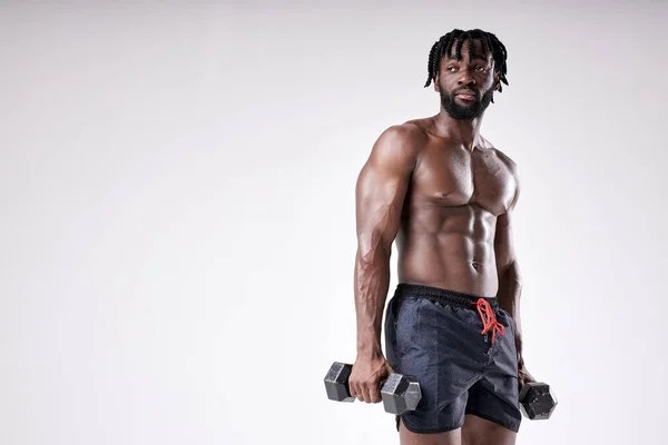 Fiatal izmos férfi súlyzókkal edz. jóképű afrikai férfi — Stock Fotó