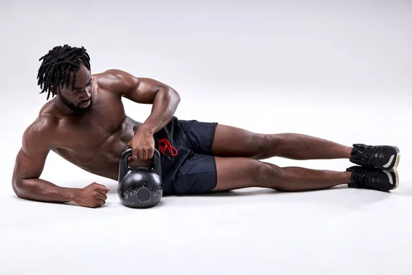 Bonito homem fitness fazendo empurrar kettlebell enquanto deitado no chão isolado no branco — Fotografia de Stock