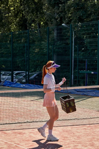 Jogadora de tênis colecionando bolas de tênis na cesta após o treino. — Fotografia de Stock