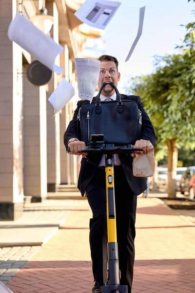 Crazy caucasian business man riding scooter in classy formal wear, hurrying at work