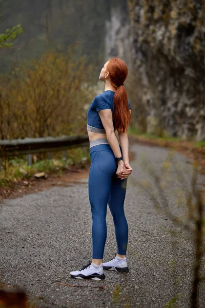 运动员红头发的女性在慢跑、跑步前伸展身体，独自在户外 — 图库照片