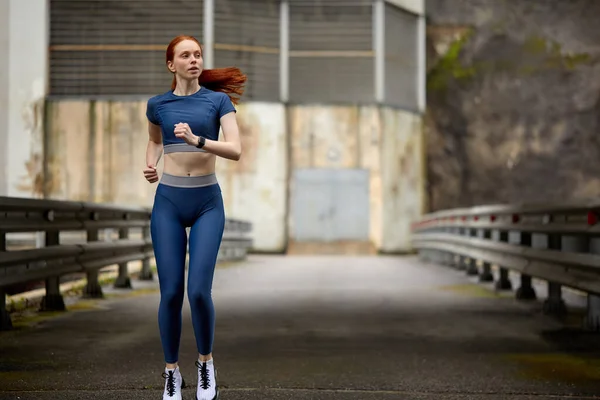 Jonge slanke roodharige vrouw opwarmen op de brug voor de training, hardlopen — Stockfoto