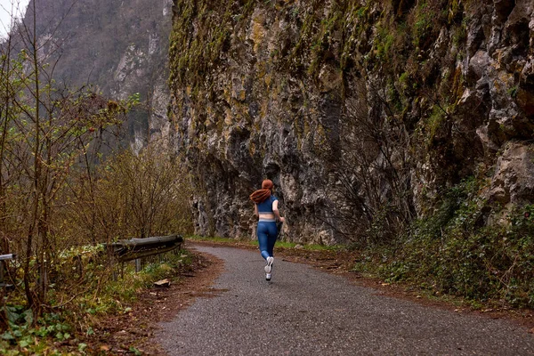 Form dağlarının yakınındaki yolda koşarak uygun kadın egzersizine arkadan bak. — Stok fotoğraf