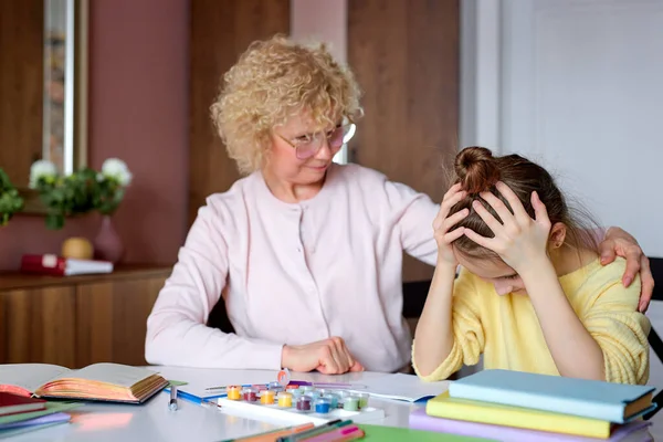 Consciente abuela sentarse con molesto hija mientras haciendo tarea, dibujo — Foto de Stock