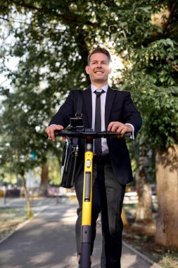 Resmi takım elbiseli neşeli beyaz iş adamı şehir caddesinde scooter kullanıyor.