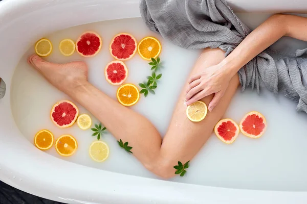 Kobieta bierze mleczną kąpiel z cytrynami i pomarańczami. Uzdrowisko cytrusowe. Opieka ciała. Wybielanie skóry — Zdjęcie stockowe