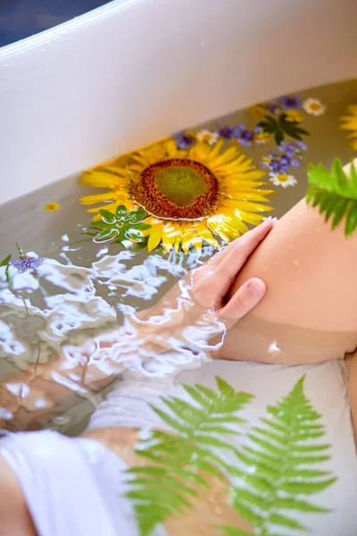 Mulher irreconhecível relaxando no banho com flores e vegetação, conceito de cuidados orgânicos da pele — Fotografia de Stock