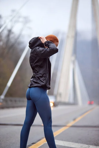 Rückansicht einer Frau in Sportbekleidung, die nach dem Lauftraining auf Brücke läuft und sich ausruht — Stockfoto