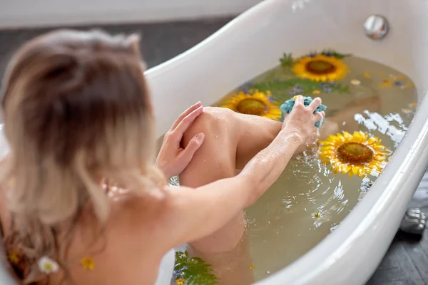 Aantrekkelijke jonge sexy vrouw met blond haar en natuurlijke make-up, neemt bad met bloemen — Stockfoto