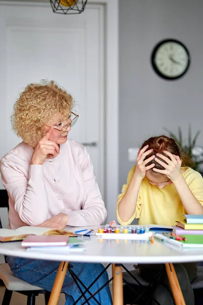 Cuidando hermosa abuela sentarse con molesto hija mientras haciendo tarea, dibujo — Foto de Stock