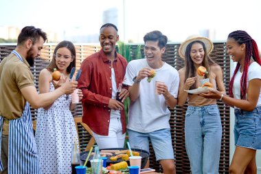 Mutlu arkadaşlar hamburger yer ve barbekü verandasında limonata içer.
