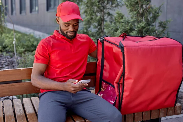 Курьер с термальным рюкзаком доставляет свежие обеды клиентам, сидит в ожидании на открытом воздухе — стоковое фото