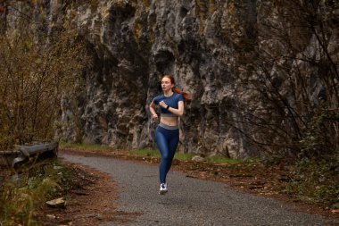 Aktif beyaz kadın, kızıl saçlı. Egzersiz yapıyor. Doğada tek başına koşuyor.