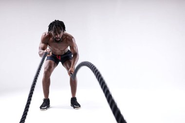 Atletik kaslı Afrikalı adam ağır iplerle çalışıyor. Beyazda izole edilmiş