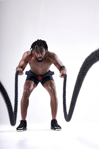 Vonzó, izmos afrikai férfi, nehéz kötelekkel edz. Fehér alapon elszigetelve — Stock Fotó