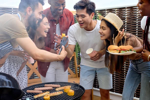 Group of friends making meal on barbecue grill, diverse people on picnic