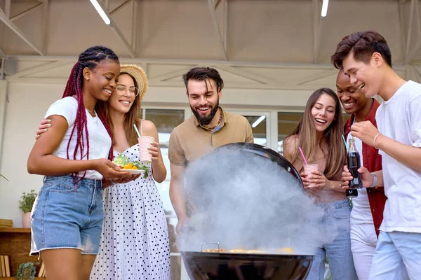 Bir grup genç arkadaş barbekü ızgarası açıyor ve akşam yemeği hazırlıyorlar. — Stok fotoğraf