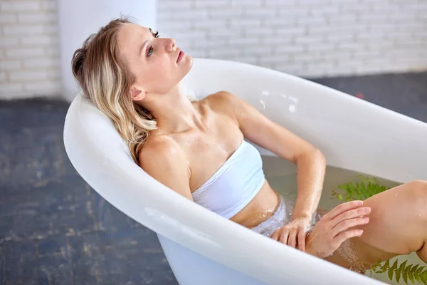 Sexy kaukasische Frau, die zu Hause mit Blumen badet. Entspannte Dame in weißer Badebekleidung — Stockfoto