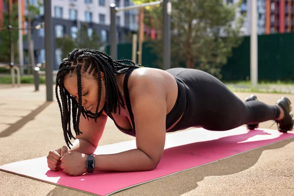 强壮肥胖的女性在室外的健身垫上做木板，侧视图肖像，聚焦 — 图库照片