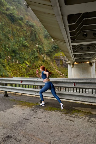 Widok z tyłu na rudych kobiet jogging sam w naturze, w niebieskich strojach sportowych — Zdjęcie stockowe