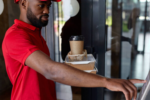 Nice takeaway delivery worker dials the apartment number in intercom of house