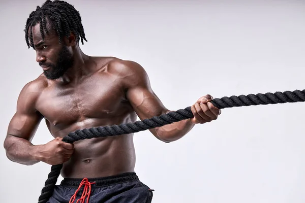 Atleta africano confiado tirando de la cuerda cruzada en forma aislada sobre fondo blanco — Foto de Stock