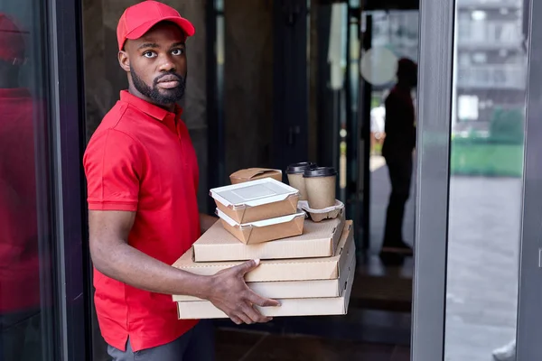 Serviço de entrega de alimentos por correio africano. Entrega homem em uniforme vermelho com caixas de pizza — Fotografia de Stock